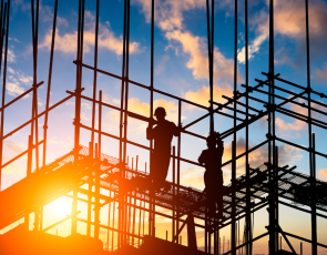 outline of construction workers on scafolding with sun behind them