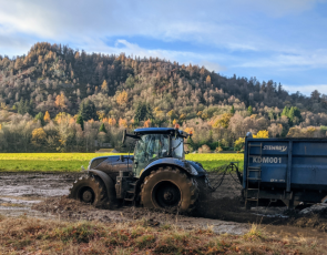 Tractpr and trailer driving through muddy field