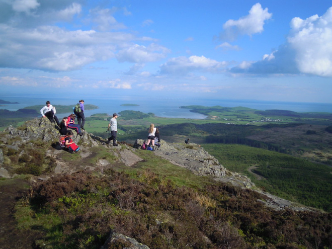 Group of teenagers on hill summit with field and sea views