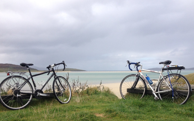 Two bikes on grassy bank overlooking sea and beach 