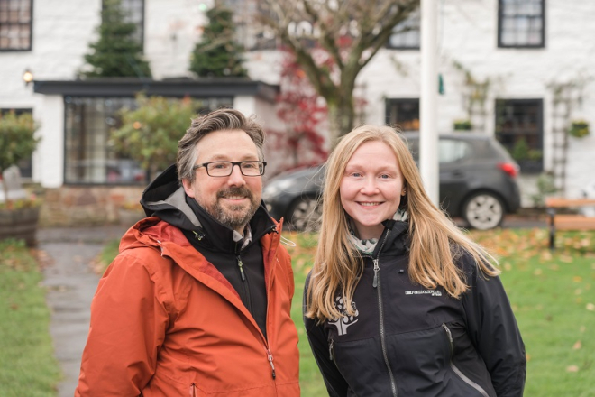 Man with beard and glasses beside woman with long blonde hair, both in outdoors clothing