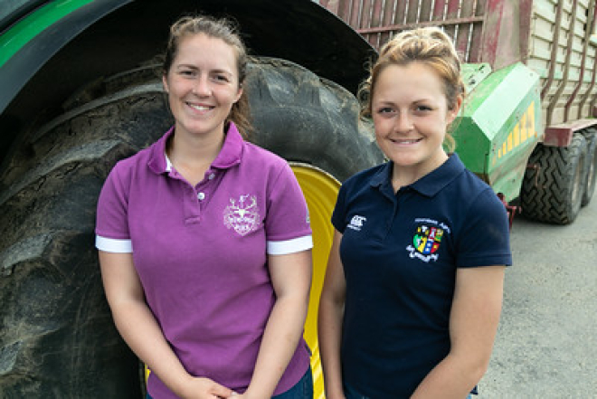 Two young women standing in front of a Green John Deere Tractor