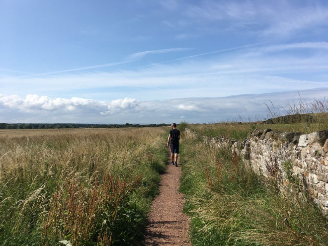 Man walking along a path in open countryside with blue skies.