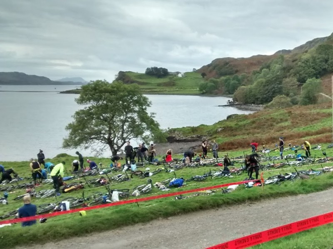 Lots of bikes laid out in a field with sea and island behind