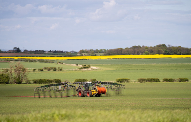 A red tractor with dribble bar spreading slurry