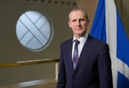 Cabinet Secretary for NHS Recovery, Health and Social Care, Michael Matheson standing in front of a Saltire flag