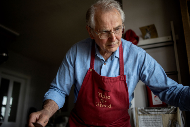 Man with white hair and glasses wearing red apron 