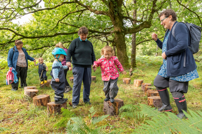 3 toddlers on stepping stones made from tree trunks in woods