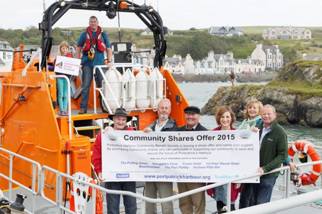 People in lifeboat in harbour with community shares banner