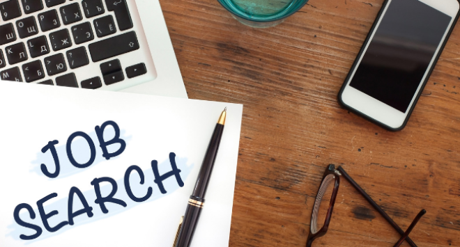 laptop, paper with 'job search' written on it, pen and phone sitting on desk