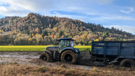 Tractpr and trailer driving through muddy field