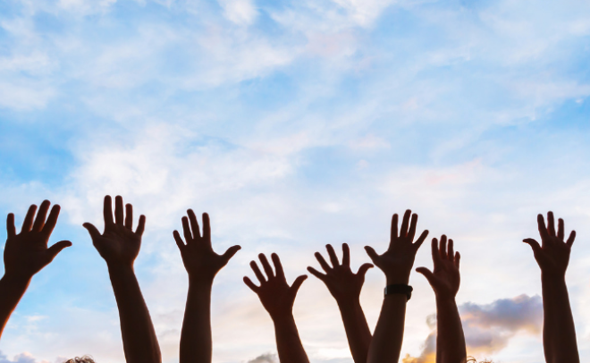 People with hands in the air against blue sky