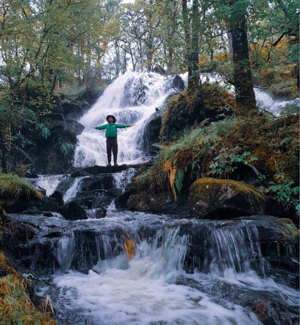 Person with arms outstretched in waterfall in woods