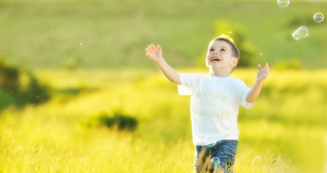 Boy chasing bubbles in field