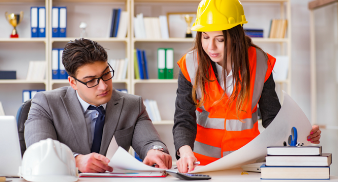 Woman with hard hat speaking to man at desk 