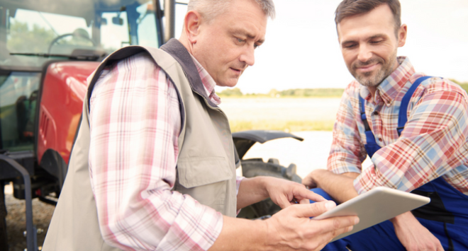 farmers looking at tablet in front of tractor