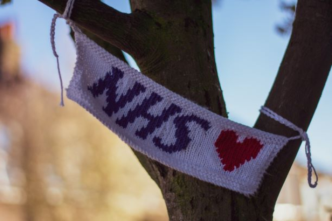 Knitted sign for NHS with a love heart tied on a tree