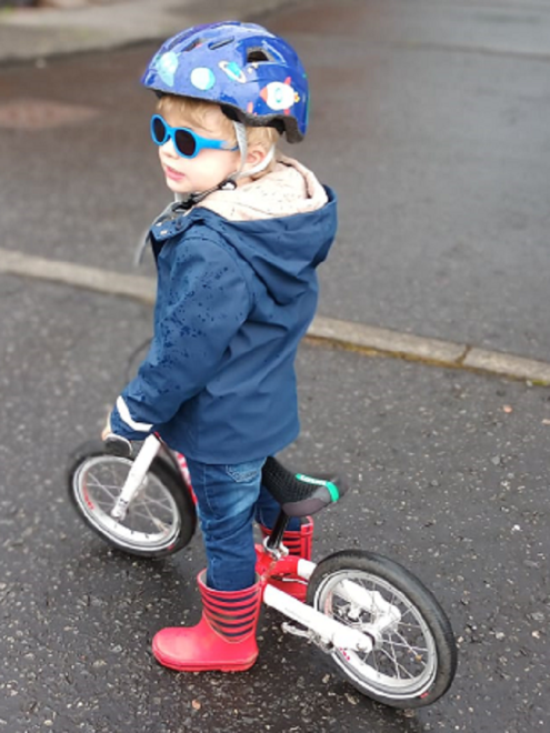 toddler wearing blue cycle helmet, sunglasses, on balance bike