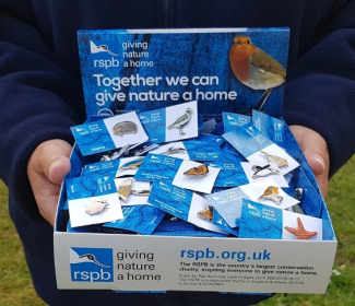 Person holding RSPB collection box with pins 